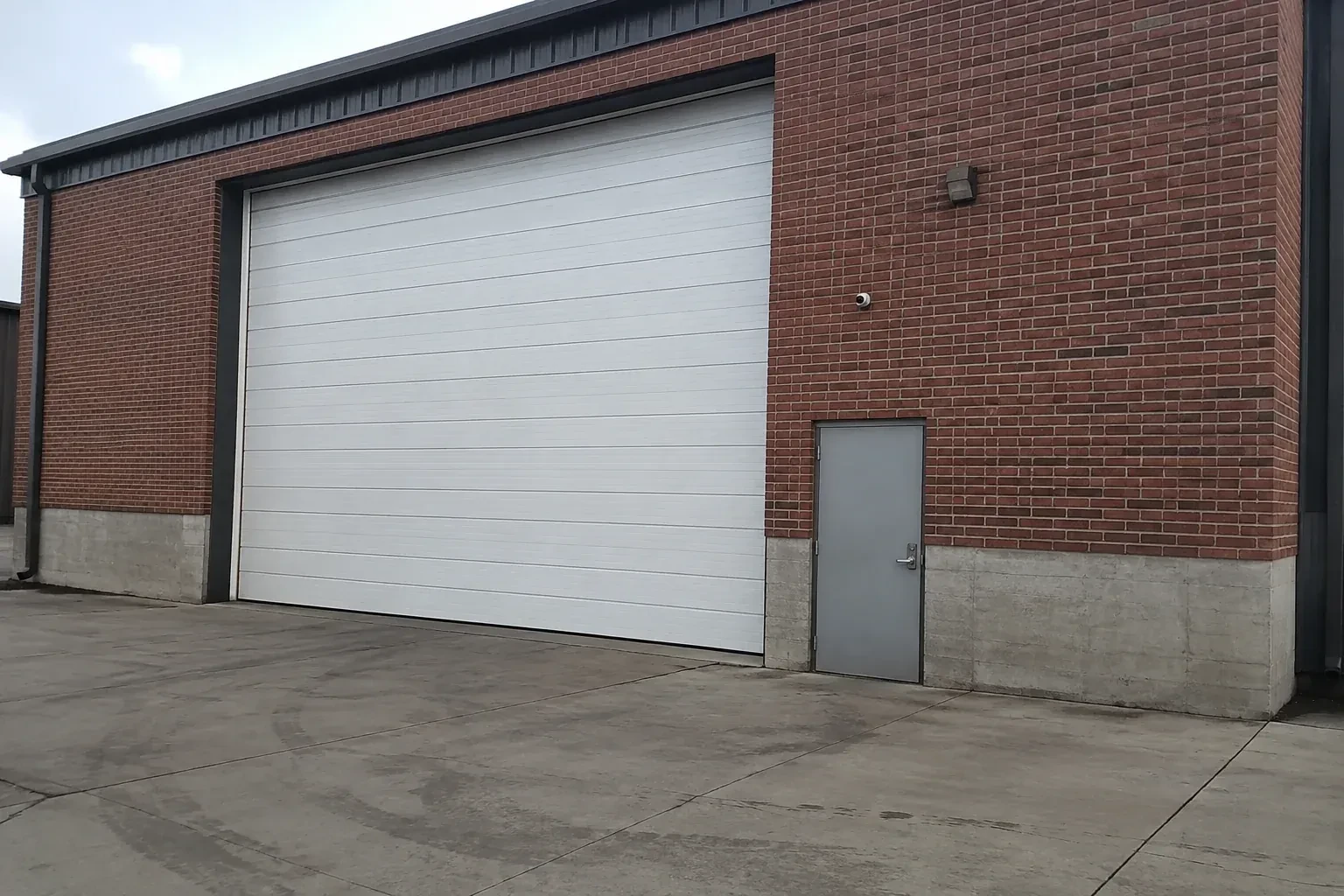 Tall closed sectional loading door beside a personnel door at a brick unit. — Commercial Sectional Door Repair, Richmond Hill