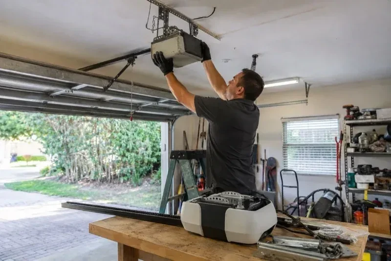 Person holding an overhead garage-door opener beside another opener and hardware on a workbench — Garage Door Opener Replacement, Richmond Hill